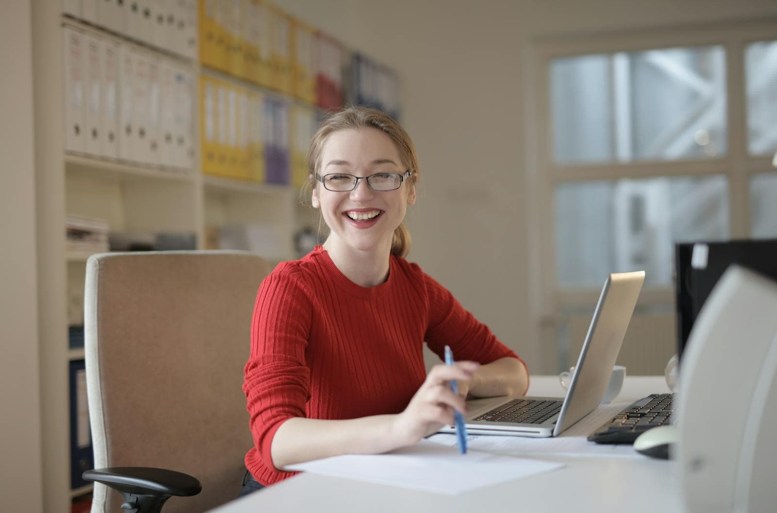 Profesional sonriendo con lapicero en mano firmando un documento desde su laptop